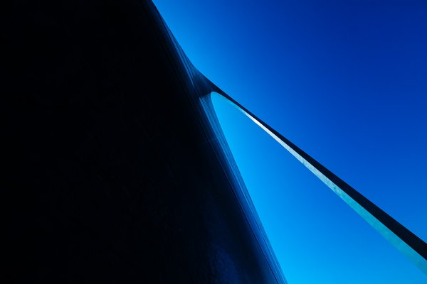 A close-up the base of the Gateway Arch in St. Louis, Missouri, agains the backdrop of a clear blue sky. The overall composition emphasizes minimalism and elegance, with the blue tones evoking a calm and futuristic atmosphere.