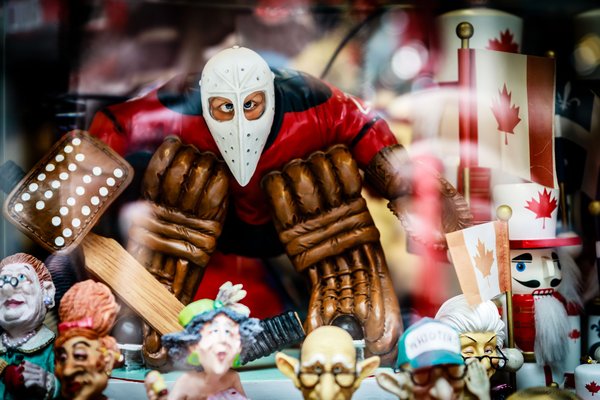 A collection of colorful figurines in a display case. The central figure is an ice hockey goalie with a white face mask. Surrounding the goalie are various characters, including royalty, a toy soldier, and a Canadian flag. The figurines are detailed and vibrant, with expressive faces and intricate costumes. The display is lively and colorful showcasing an overall theme of Canadian pride.