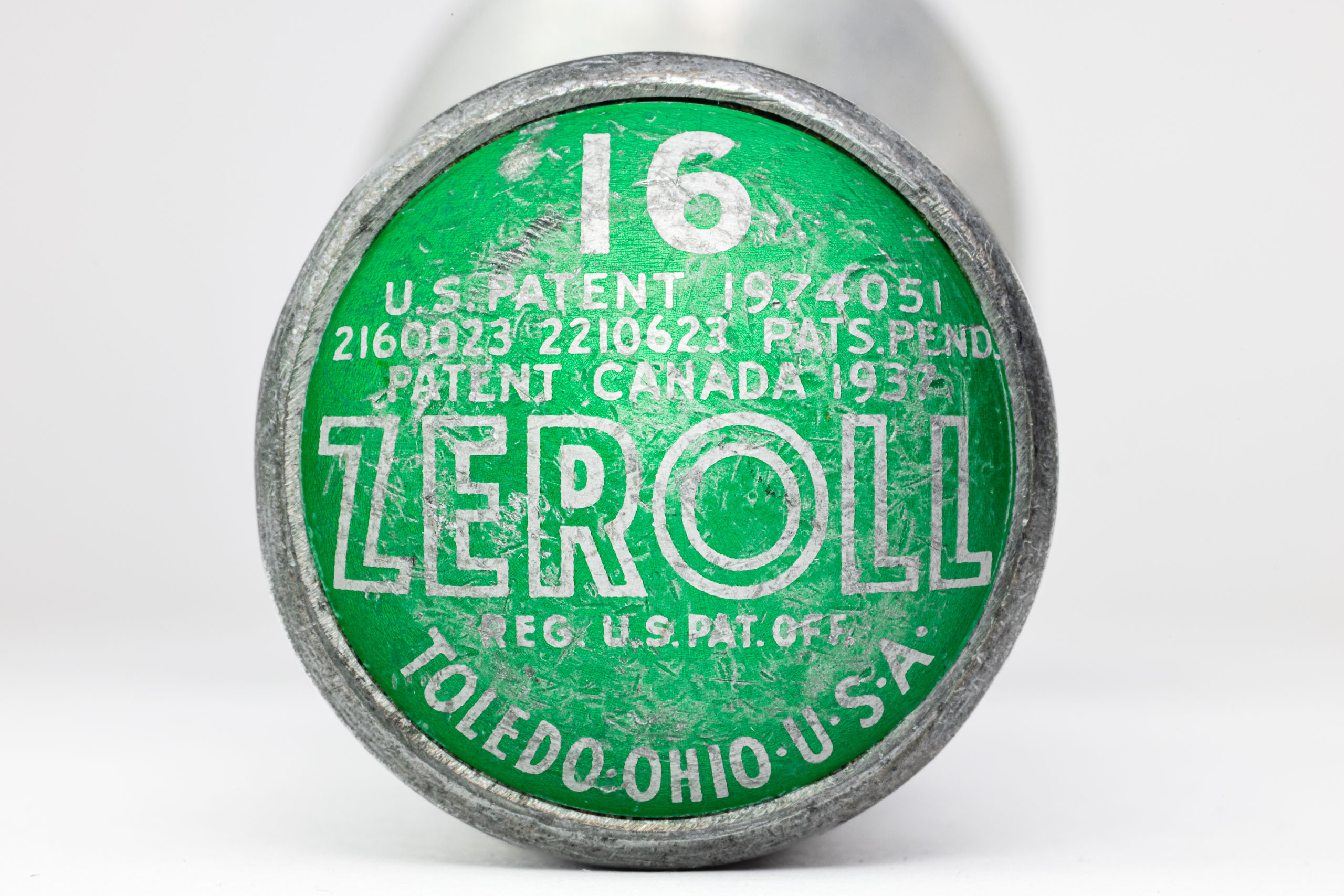 A round, green and silver end of an ice cream scoop with worn-off text. The text includes "ZEROLL," "TOLEDO, OHIO, U.S.A.," and patent numbers. The number "16" is prominently displayed in white. The surface shows signs of age and wear, with scratches and faded areas.