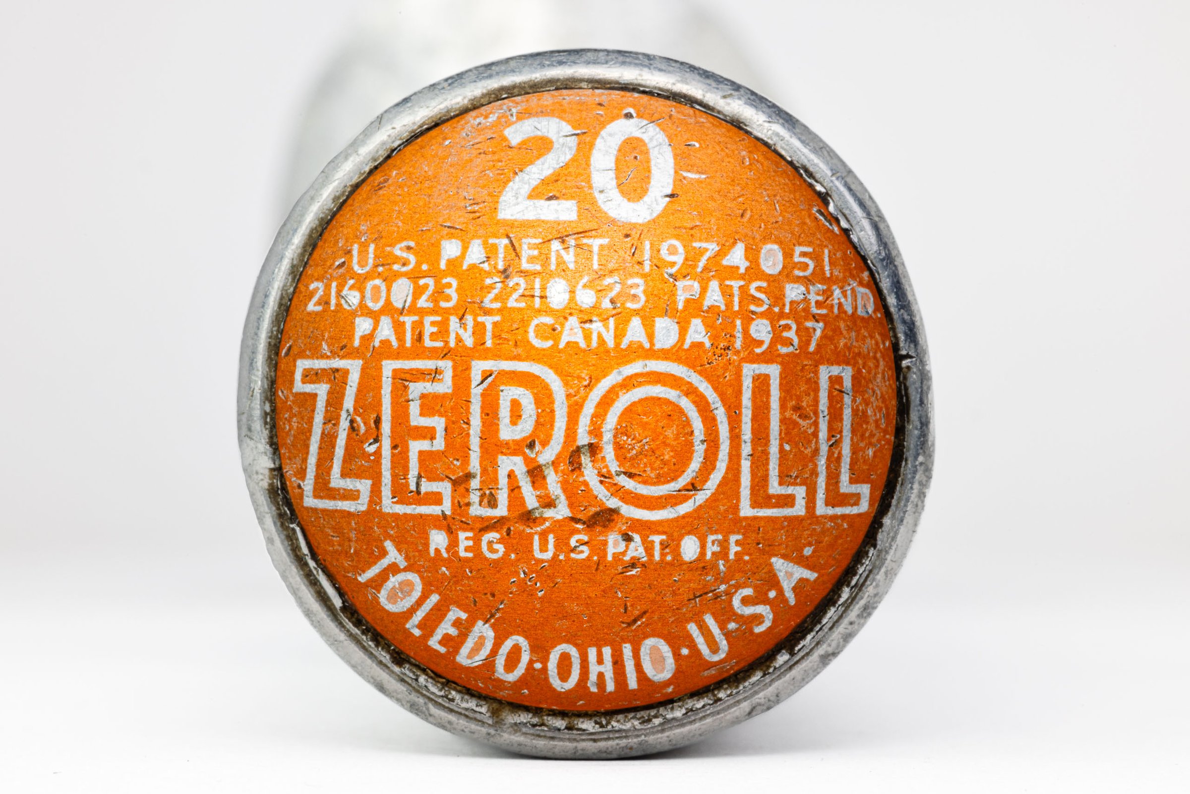 A round, orange and silver end of an ice cream scoop with worn-off text. The text includes "ZEROLL," "TOLEDO, OHIO, U.S.A.," and patent numbers. The number "20" is prominently displayed in white. The surface shows signs of age and wear, with scratches and faded areas.
