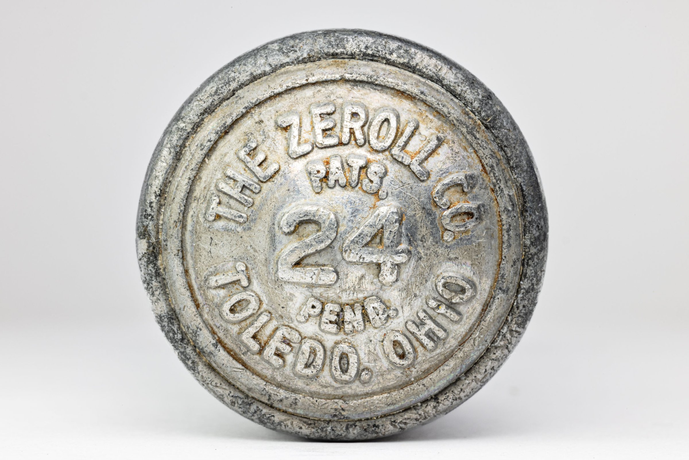 A round, silver end of an ice cream scoop with worn-off text. The text includes "ZEROLL," "TOLEDO, OHIO, U.S.A.," and "PATS. PEND.". The number "24" is prominently displayed in the center. The surface shows signs of age and wear, with scratches and faded areas.