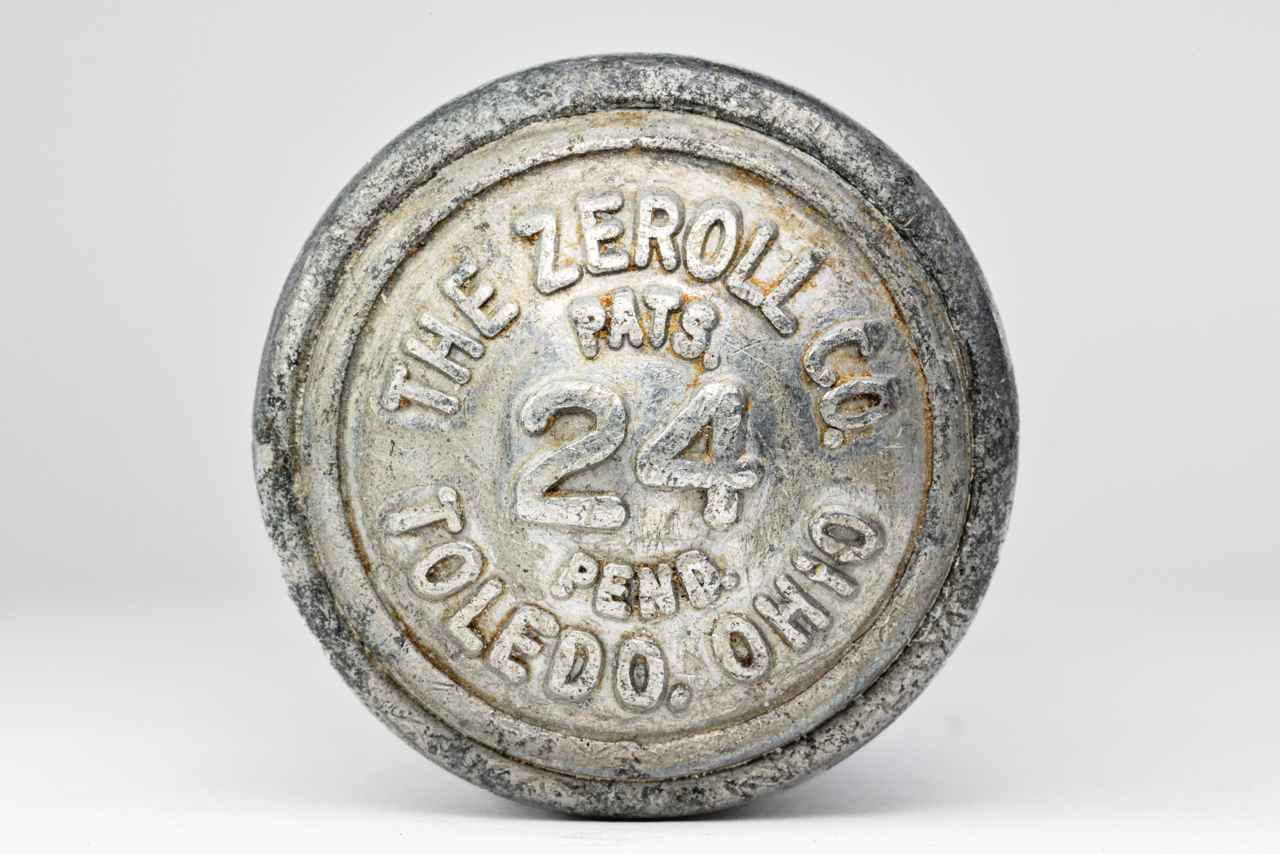 A round, silver end of an ice cream scoop with worn-off text. The text includes "ZEROLL," "TOLEDO, OHIO, U.S.A.," and "PATS. PEND.". The number "24" is prominently displayed in the center. The surface shows signs of age and wear, with scratches and faded areas.