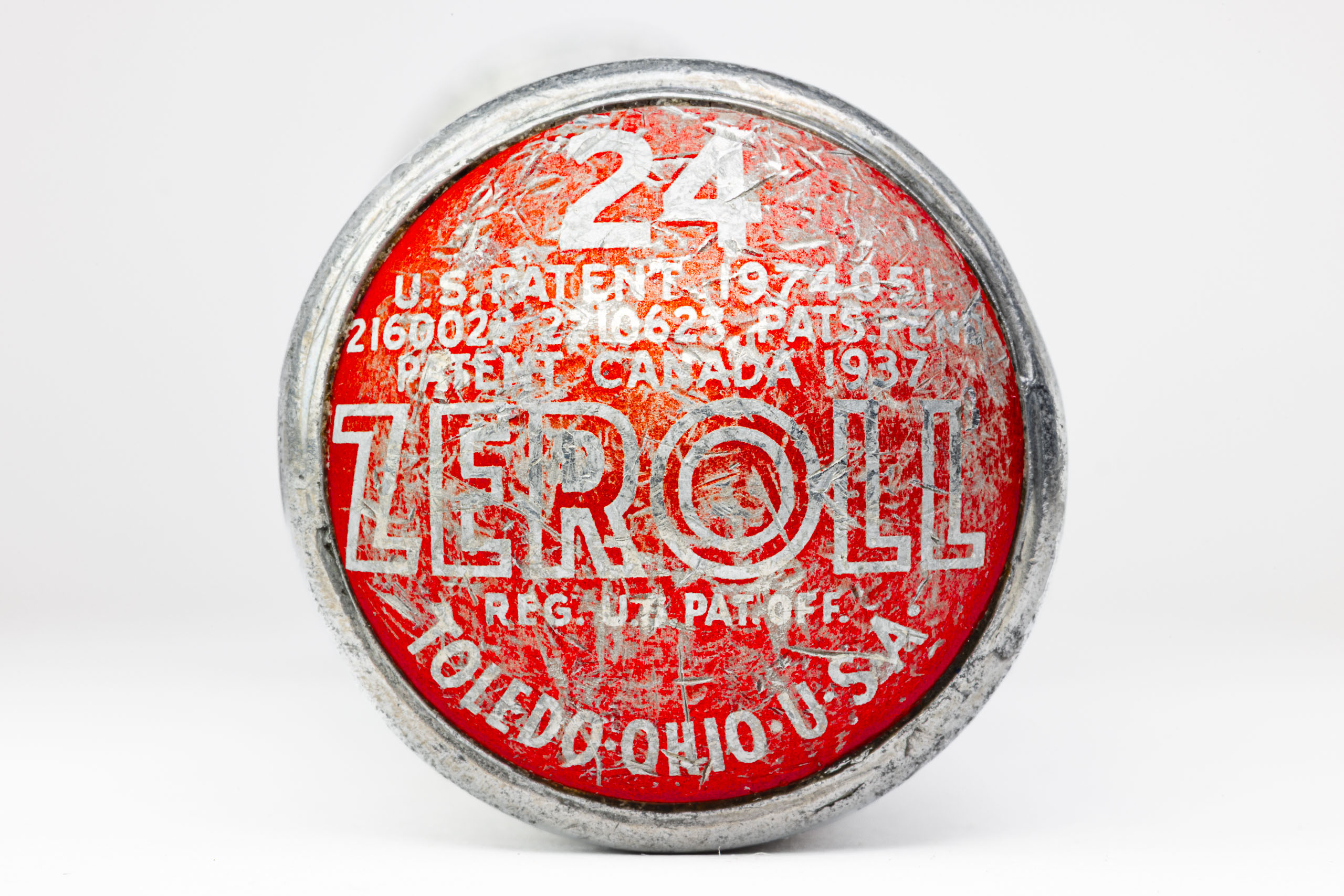 A round, red and silver end of an ice cream scoop with worn-off text. The text includes "ZEROLL," "TOLEDO, OHIO, U.S.A.," and patent numbers. The number "24" is prominently displayed in white. The surface shows signs of age and wear, with scratches and faded areas.