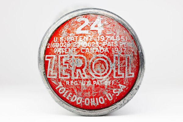 A round, red and silver end of an ice cream scoop with worn-off text. The text includes "ZEROLL," "TOLEDO, OHIO, U.S.A.," and patent numbers. The number "24" is prominently displayed in white. The surface shows signs of age and wear, with scratches and faded areas.